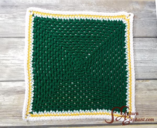 Crocheted small green square blanket with white and yellow border.