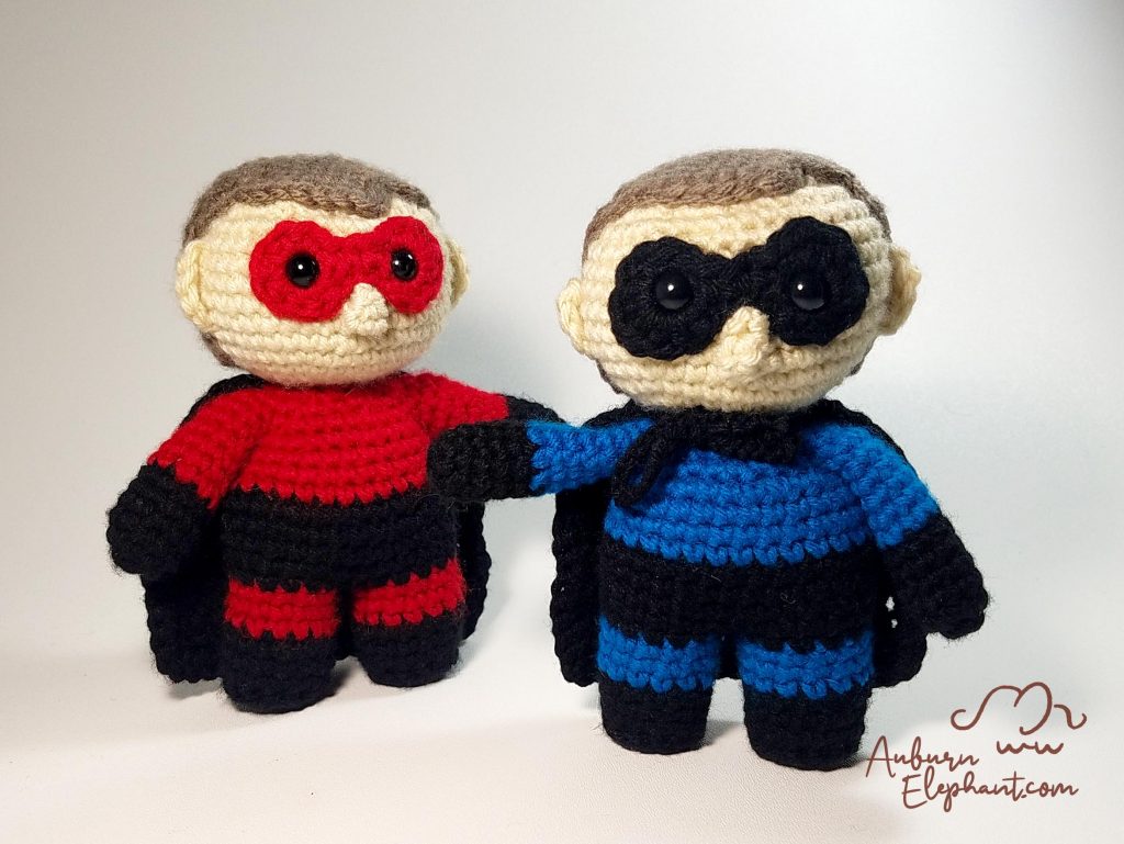A pair of Little Super Hero dolls stand side by side in red and blue.